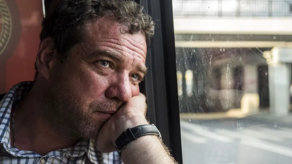 Man resting head on palm looking outside of window