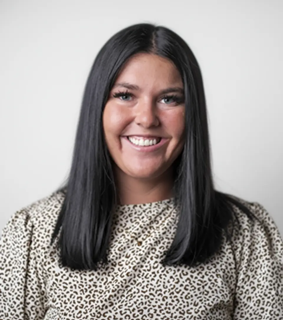 Smiling professional woman with shoulder-length dark hair dressed in a patterned top, photographed against a white backdrop.